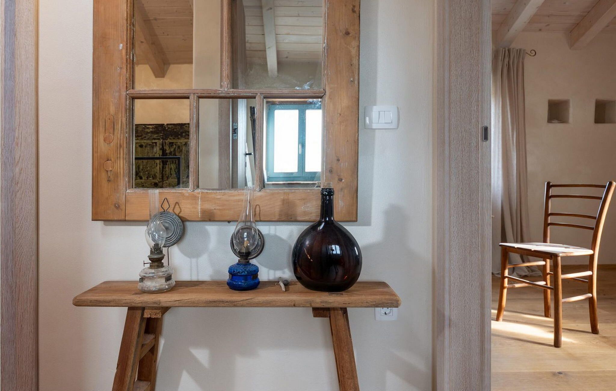 Une table en bois, avec un miroir au-dessus, un vase foncé et deux luminaires.
