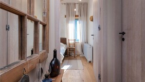 A narrow hallway with wooden walls and doors, leading to a bedroom with a bed, chair, and window with curtains. - Gorgeous home in Porec (Porec)
