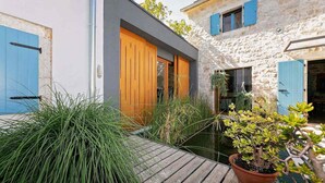 A courtyard with a wooden deck, a potted plant, and a stone building with blue shutters. - Gorgeous home in Porec (Porec)