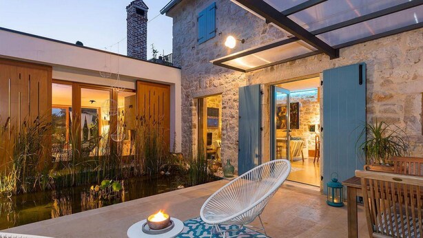 A cozy outdoor seating area with a fire feature, a stone building with a wooden door, and a view of a pond. - Gorgeous home in Porec (Porec)