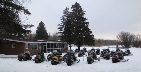 A snow-covered area with several snowmobiles parked in front of a building. - Cabin 11 Lakefront Family Resort (Hines)