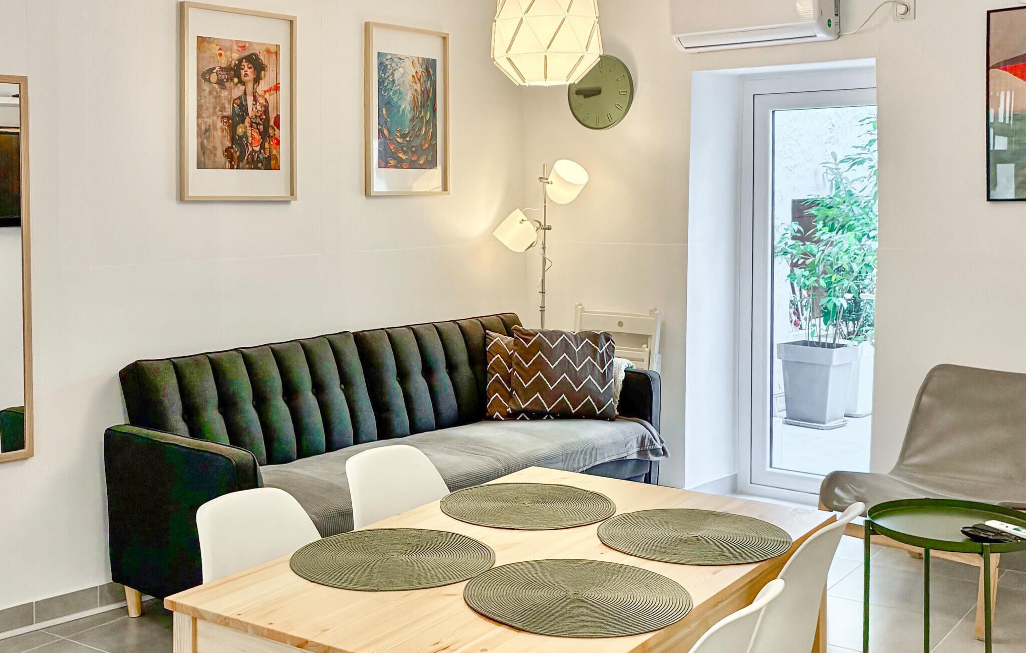 Ein modernes Wohnzimmer mit einer Couch, einem Esstisch, Stühlen, Kunstwerken und Blick durch eine Glastür.