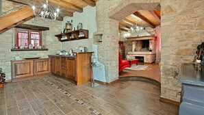 A rustic kitchen with wooden cabinets, a stone wall, and a fireplace.