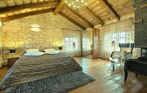 A spacious bedroom with a stone wall, wooden ceiling beams, a large bed, a glass table, and a chair. - Cozy home in Umag with sauna (Umag)