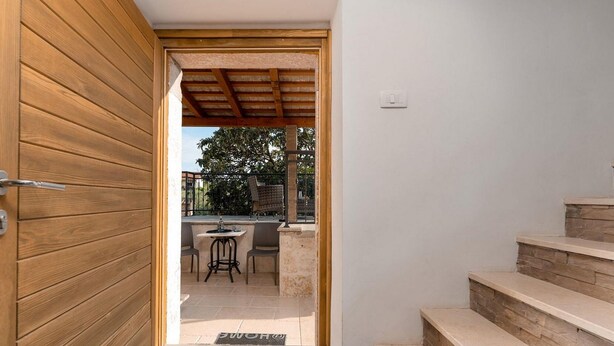 A wooden door leading to an outdoor patio area with a table and chairs, a stone staircase, and a view of trees.