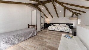 A bedroom with a wooden ceiling, a bed with a floral duvet, a bedside table, and a small seating area with a magazine.