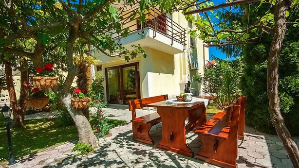 A patio with a wooden table and benches, surrounded by potted plants and trees. - 2 bedroom beautiful home in Labin (Labin)