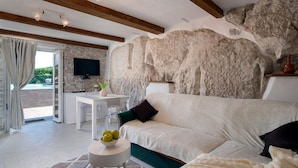 Een moderne woonkamer met een stenen muur, een witte bank, een klein tafeltje met appels en een televisie aan een stenen muur.