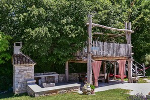 A rustic outdoor kitchen with a stone chimney, a dining area with a table and chairs, and a wooden swing set. - Holiday apartment mit Pool und Klimaanlage (Modrušani)