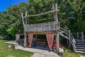 En rustik trækonstruktion med balkon, stenbænk og gyngestativ.