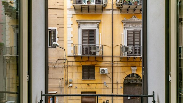 A yellow building with balconies, a car parked in front, and a metal railing in the foreground.