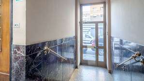 Un couloir aux murs de marbre, une porte donnant sur l’extérieur et un panneau vert indiquant la sortie de secours.