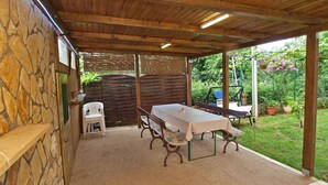 A covered patio area with a stone wall, a table with chairs, and a garden with potted plants and flowers. - Holiday apartment with air conditioning (Fažana)