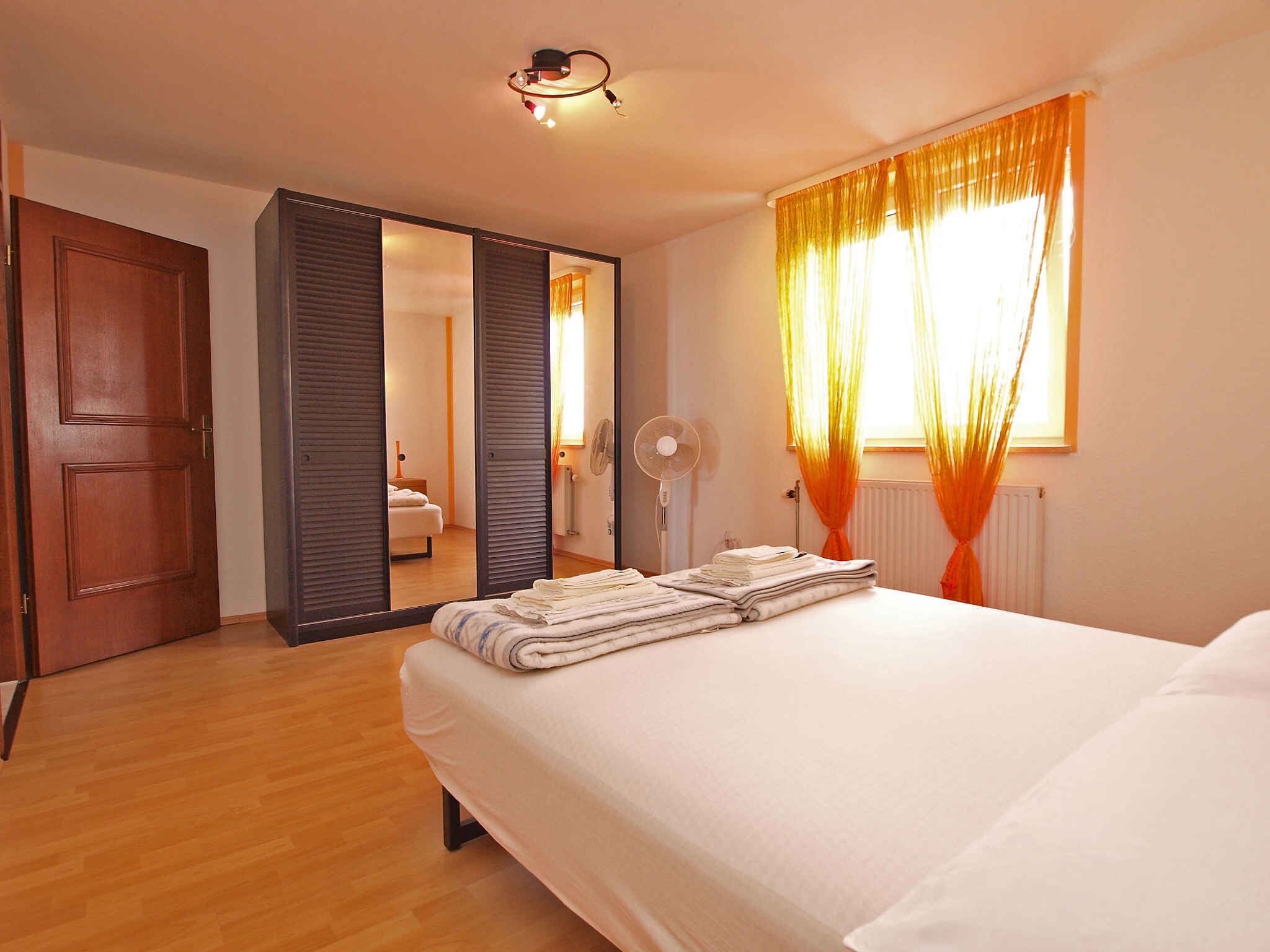 Une chambre d’hôtel avec un lit, un plancher en bois, une armoire, un miroir et une fenêtre avec des rideaux.
