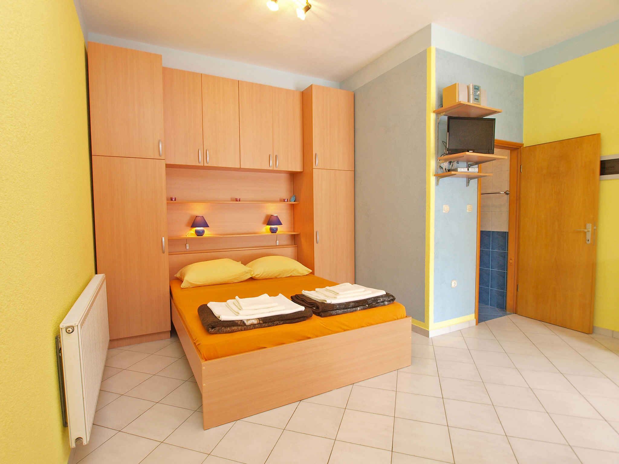 Un dormitorio con cama, armarios de madera, radiador, estante con lámparas y televisor.