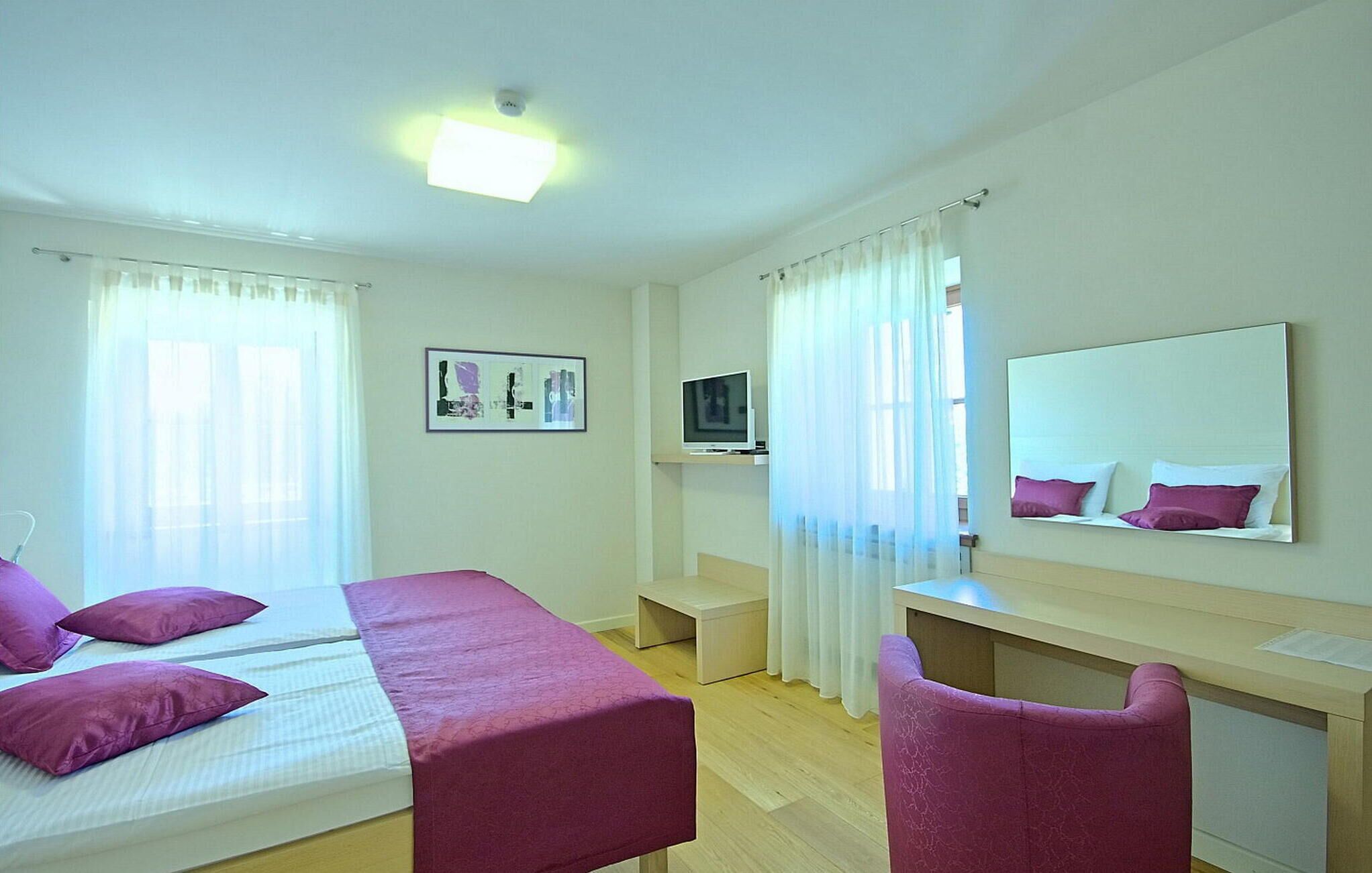 A hotel room with a bed, a desk, a chair, a television, and a mirror.