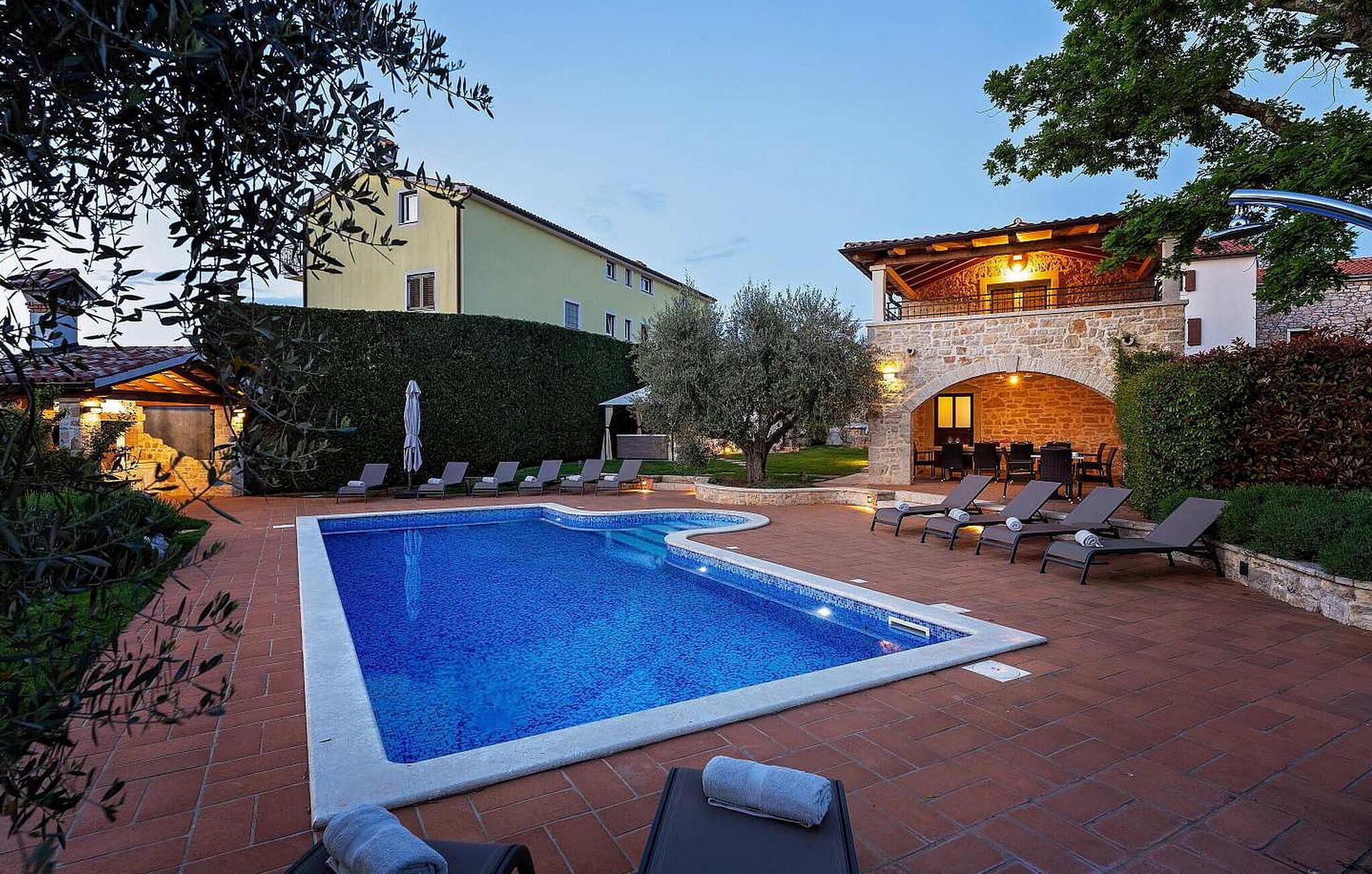 Ein Swimmingpool mit Liegestühlen und einer Außenbereich-Sitzgelegenheit, umgeben von Gebäuden und Grünflächen.