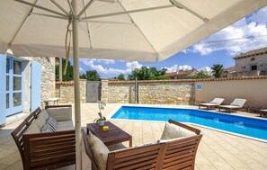 Relax by the pool surrounded by a shaded area with a wooden deck, table, and lounge chairs.