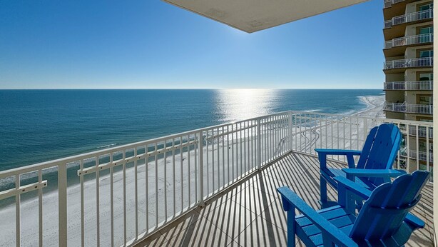 A balcony with a view of the ocean and beach, featuring blue chairs and a railing.