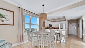 A spacious kitchen with white cabinetry, a dining area with a round table and chairs, and a large window offering a view of the sky.