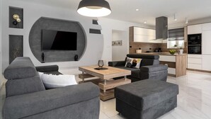 Una sala de estar moderna con sofás grises, una mesa de centro de madera y un televisor de pantalla plana montado en la pared.