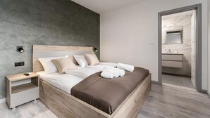 Un dormitorio moderno con una cama de madera, mesitas de noche y un baño visible a través de una puerta abierta.