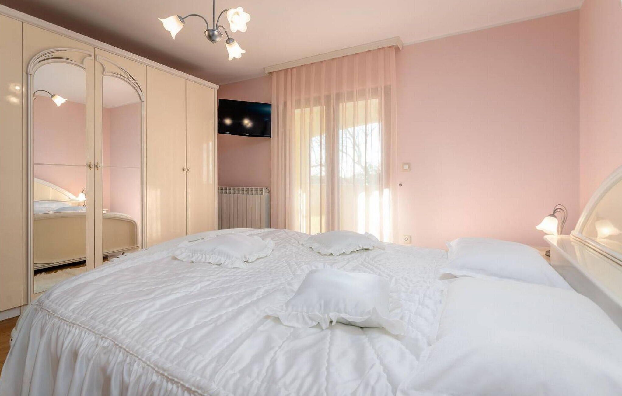 A bedroom with a large bed, a wardrobe, a television, and a window with curtains.