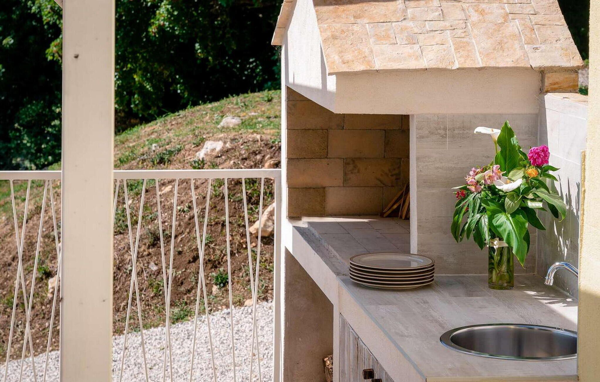 A small outdoor kitchen with a stone backsplash, a sink, and a potted plant.