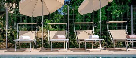 Ein Poolbereich mit vier Liegestühlen und zwei Sonnenschirmen.