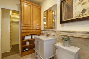 Bathroom features a vanity, sink, and mirror, with a framed artwork on the wall and a potted plant.
