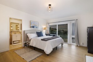 Relax in a serene space with a large bed, nightstand, and dresser, and enjoy a view of the outdoors through the large window.