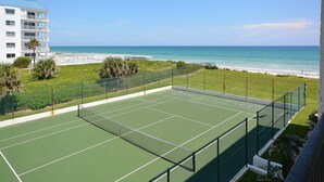 Una cancha de tenis con vista al océano y un edificio al fondo.