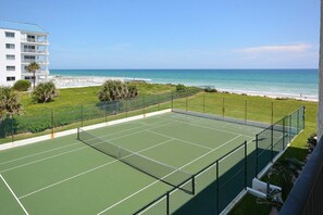 A tennis court with a view of the ocean and a building in the background.