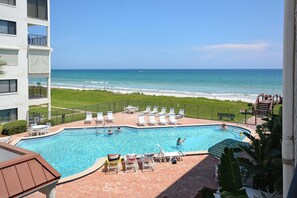 A swimming pool with lounge chairs, a view of the ocean, and a grassy area.