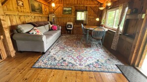 A cozy cabin interior with a wooden ceiling, a sofa with cushions, a dining table with chairs, and a patterned rug. - The Pond Cabin at Sky Hollow, The Hunter Cabin at Sky Hollow (Rochester)