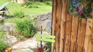 A wooden deck with a green metal table and chairs, a rustic wooden wall with a decorative painting, and a garden view. - The Pond Cabin at Sky Hollow, The Hunter Cabin at Sky Hollow (Rochester)