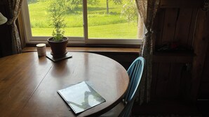 A wooden table with a notebook and a potted plant, a chair, and a window with curtains. - The Pond Cabin at Sky Hollow, The Hunter Cabin at Sky Hollow (Rochester)