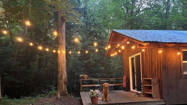 A rustic cabin with a wooden deck, surrounded by trees. - The Creek Cabin at Sky Hollow, The Creek Cabin at Sky Hollow (Rochester)