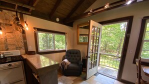 A cozy kitchen with a stove, a dining area with a chair, and a view of the outdoors through a glass door. - The Creek Cabin at Sky Hollow, The Creek Cabin at Sky Hollow (Rochester)