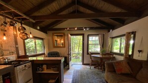 A cozy kitchen with a stove, sink, and hanging pots. There is a dining area with a table and chairs, and a living room with a couch. - The Creek Cabin at Sky Hollow, The Creek Cabin at Sky Hollow (Rochester)
