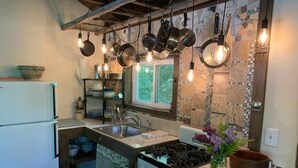 A kitchen with a built-in stove, a sink, and hanging pots. There is a window above the sink and a refrigerator on the left. - The Creek Cabin at Sky Hollow, The Creek Cabin at Sky Hollow (Rochester)