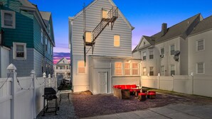 Un quartier résidentiel avec une maison blanche dotée d’une échelle de secours, d’un barbecue et d’un espace salon extérieur.
