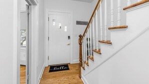 Un couloir blanc avec un escalier en bois, une pancarte de bienvenue et un paillasson sur lequel est écrit « bonjour ».