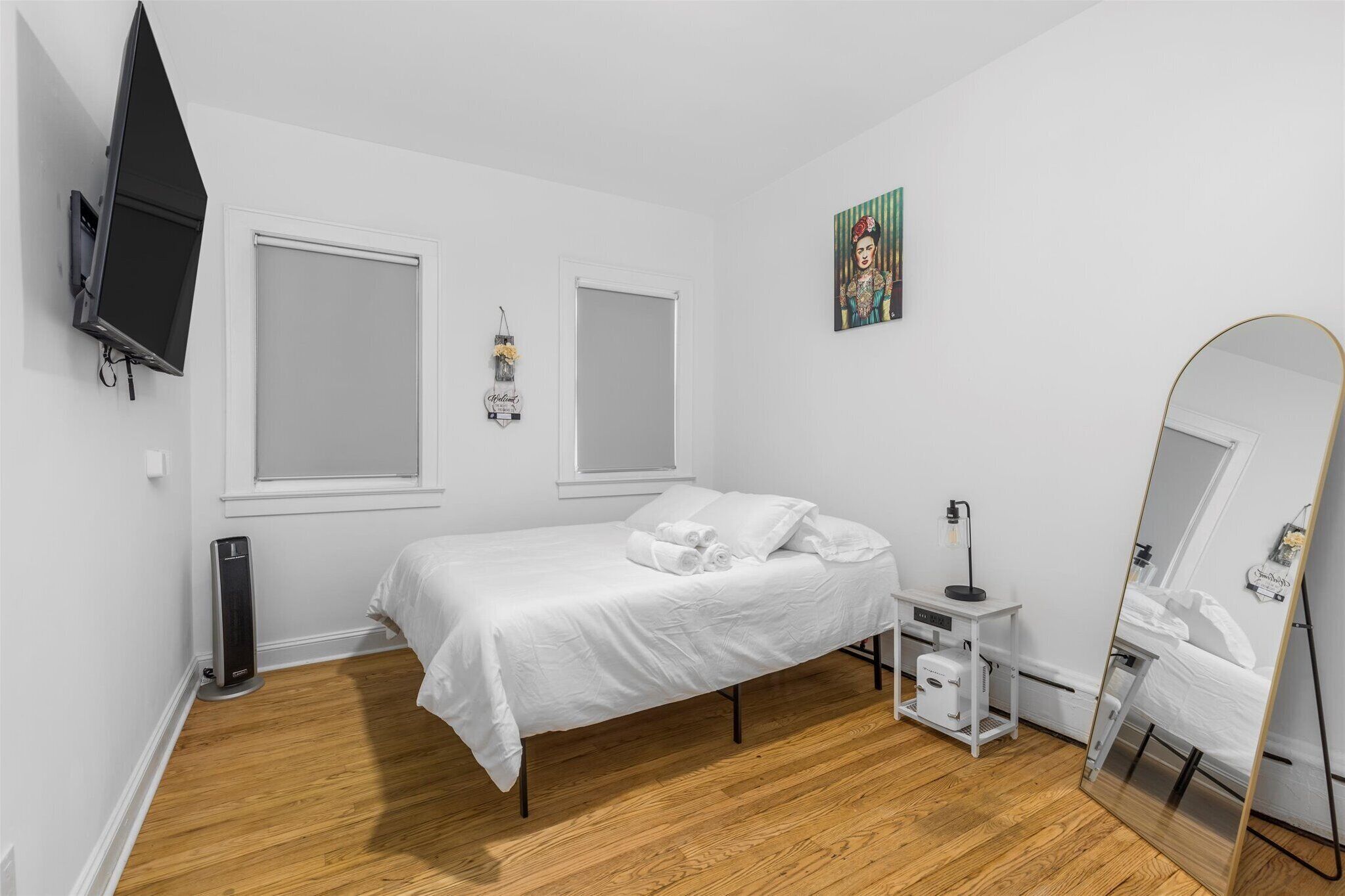 Una camera da letto con un letto, un comodino, uno specchio, una TV fissata al muro e una finestra.