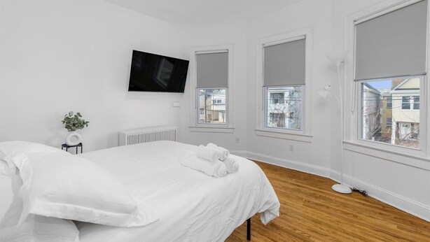 Une chambre à coucher avec un lit, un téléviseur fixé au mur et de grandes fenêtres équipées de stores.