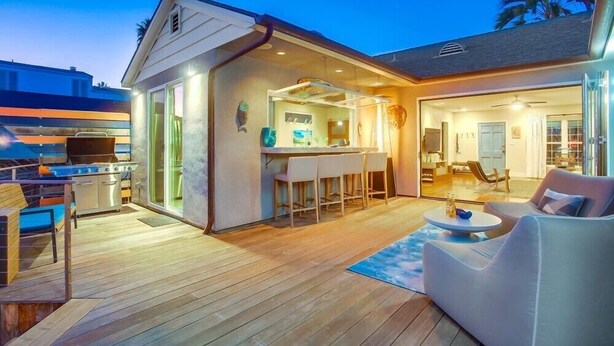 A modern outdoor living area with a barbecue, a bar, and a seating area with a sofa and a round table. - Amazing Beach House! 2 Yards w/ Hot Tub + Fire Pit (San Diego)