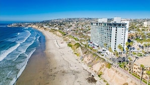A coastal hotel with a beachfront view, a large building with multiple floors, and a sandy beach. - Amazing Beach House! 2 Yards w/ Hot Tub + Fire Pit (San Diego)
