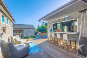 An outdoor bar area with a pool, bar stools, and a seating area with a table and chairs.