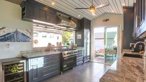 A modern kitchen with dark cabinetry, a large island, and a built-in oven. - Amazing Beach House! 2 Yards w/ Hot Tub + Fire Pit (San Diego)