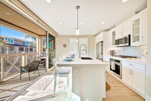 A modern kitchen with a central island, white cabinetry, and a view to a covered outdoor area.